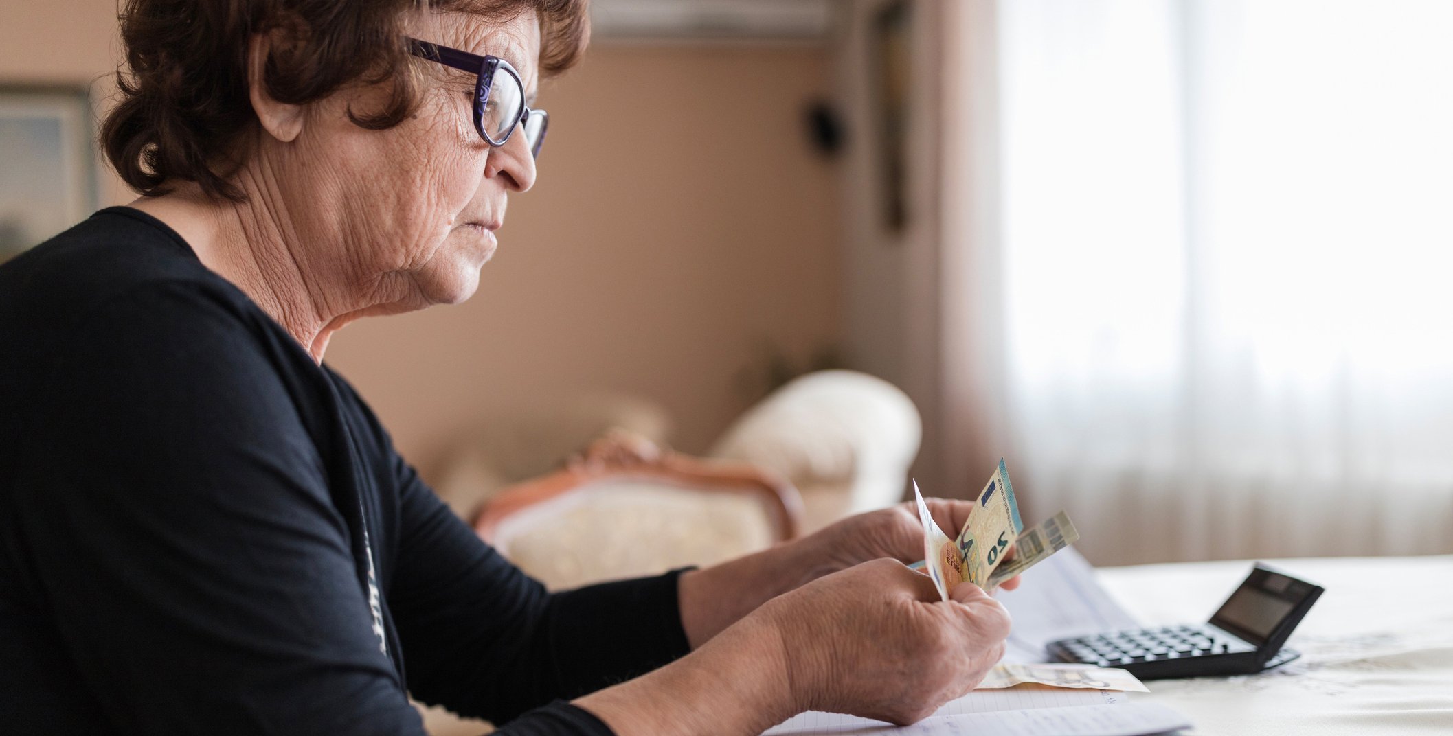 Eine Frau sitzt an einem Tisch und zählt Geld, auf dem Tisch liegt ein Taschenrechner